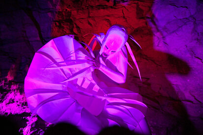 Foto einer Aufführung: eine weiße Figur im pinken Licht.