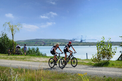 Foto: Zwei Radfahrer fahren am See vorbei.